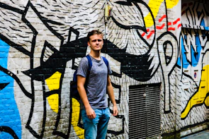 Young model wearing a modern t-shirt with abstract design, posing against a graffiti wall.