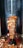 A vertical stack of marinated meat slices is cooking on a rotating spit, commonly found in Middle Eastern cuisine. The meat appears to be juicy and cooked, with crispy edges, surrounded by heat and a metal grill.