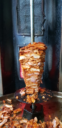 Close-up of sizzling döner meat rotating on a vertical spit with warm lighting.