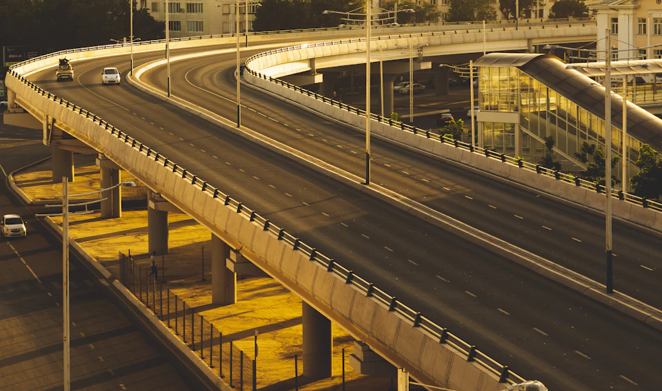 Large curved highway overpass with multiple lanes and pedestrian walkway under bridge structure