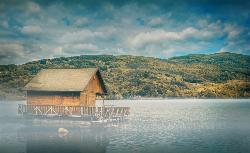 Cabaña flotante de madera marrón en medio del cuerpo de agua con la montaña en el fondo