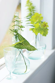 A delicate hanging glass flower vase catching sunlight among green garden leaves.