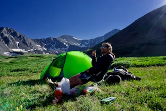 man sitting on black camping chair beside green dome tent