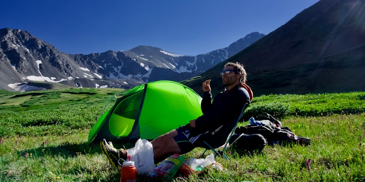 man sitting on black camping chair beside green dome tent