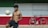 A shirtless young man balances a soccer ball on his knee in an outdoor setting with a large horizontal tricolor wall of green, white, and red. To the right, against the wall, is a parked black bicycle with a brown seat and handlebars.