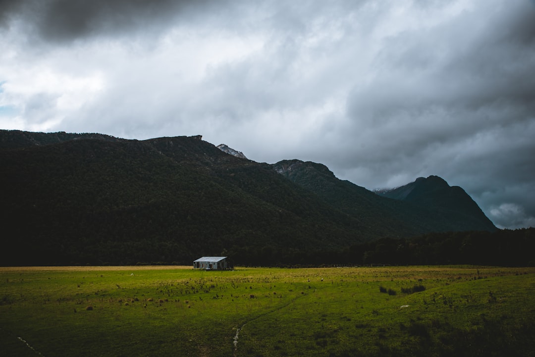 landscape photography of grey wooden house on grass field and mountains in distance during daytime