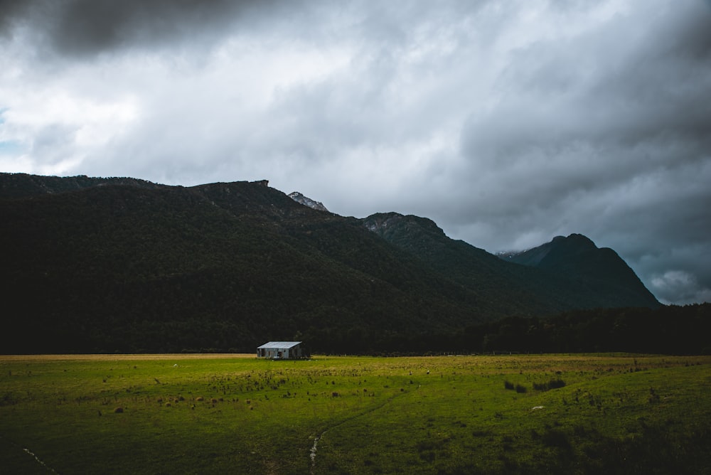 photographie de paysage de maison en bois gris sur un champ d’herbe et des montagnes au loin pendant la journée