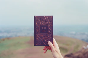 Close-up of a hand holding a classic book with modern graffiti art on its cover