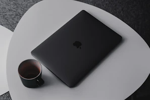 A modern laptop and coffee cup on a sleek black table with shadows