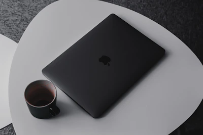 Minimalist c-shaped side table next to a modern sofa with a laptop and coffee cup on top.