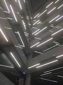 An architectural design featuring multiple levels of staircases and landings, illuminated by bright linear lights. The composition creates geometric patterns and lines, with glass and metal surfaces reflecting light to add depth.