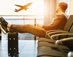 man sitting on gang chair with feet on luggage looking at airplane