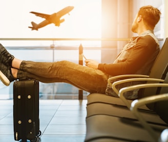 man sitting on gang chair with feet on luggage looking at airplane