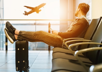 man sitting on gang chair with feet on luggage looking at airplane