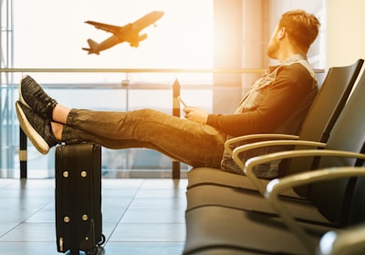 man sitting on gang chair with feet on luggage looking at airplane