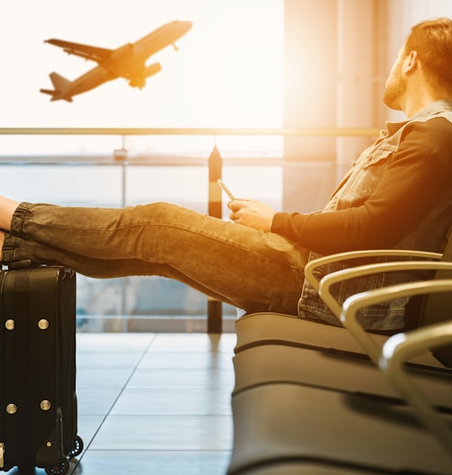 man sitting on gang chair with feet on luggage looking at airplane