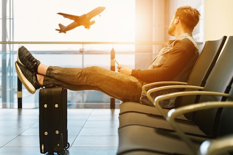 man sitting on gang chair with feet on luggage looking at airplane