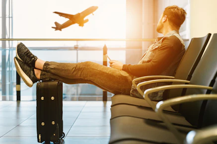 man sitting on gang chair with feet on luggage looking at airplane