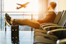 man sitting on gang chair with feet on luggage looking at airplane