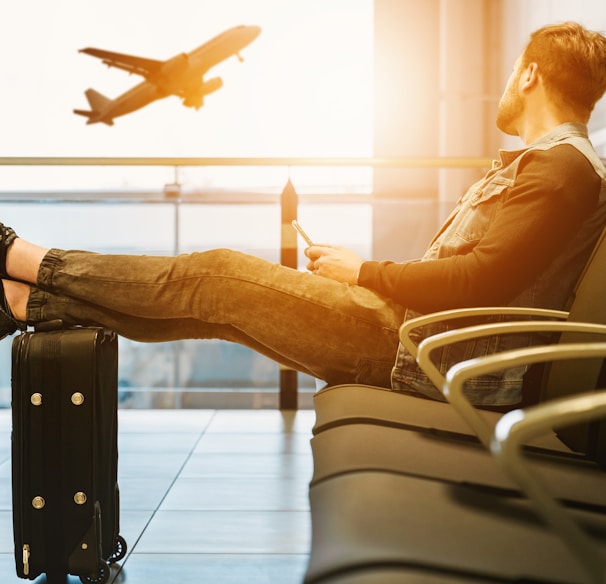 man sitting on gang chair with feet on luggage looking at airplane