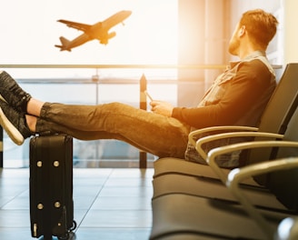 man sitting on gang chair with feet on luggage looking at airplane