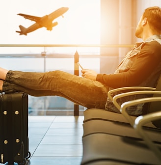 man sitting on gang chair with feet on luggage looking at airplane