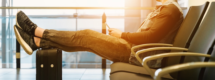 man sitting on gang chair with feet on luggage looking at airplane