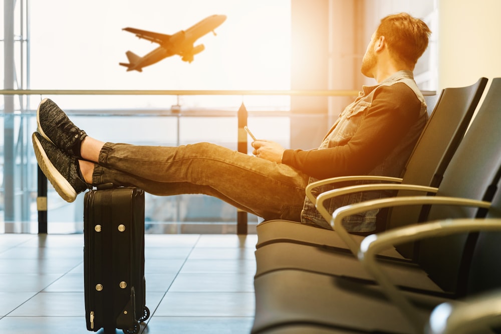 homme assis sur une chaise de gang avec les pieds sur les bagages regardant l’avion