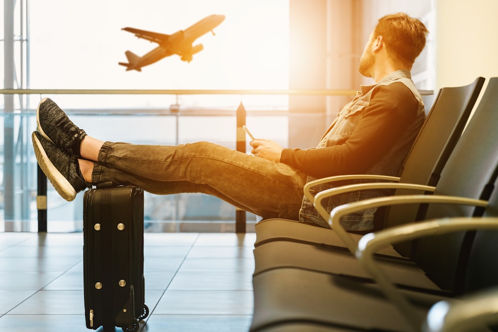 homem sentado na cadeira da gangue com os pés na bagagem olhando para o avião