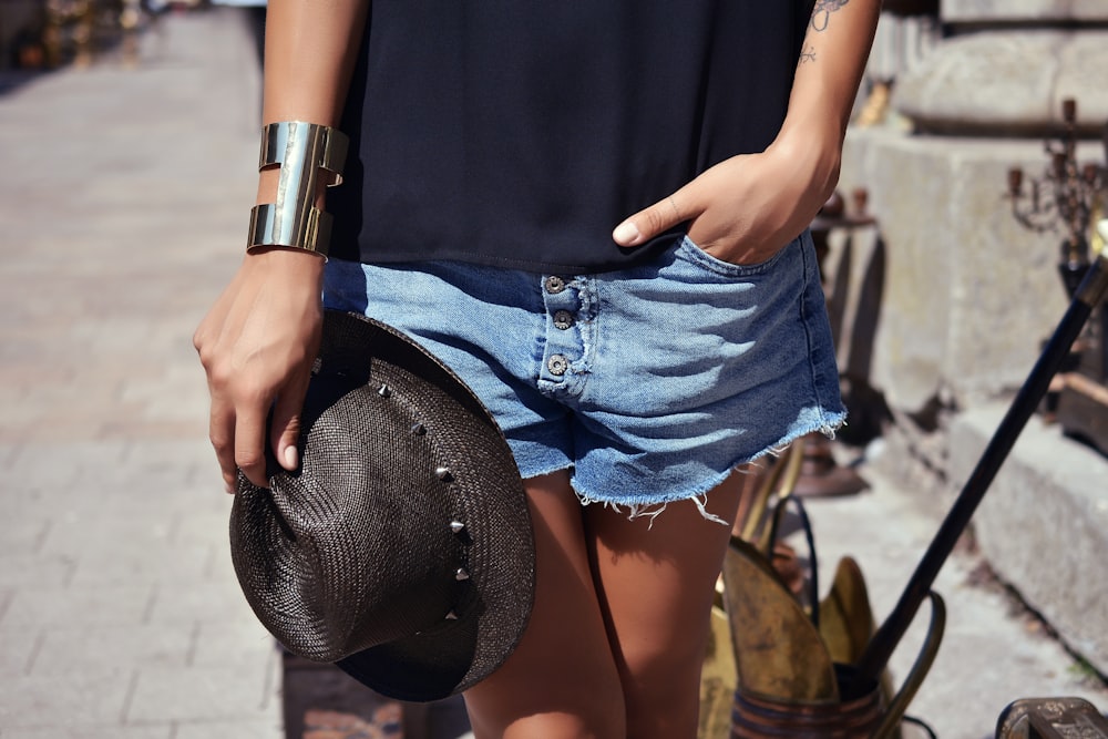 person wearing blue denim short shorts and holding black trilby hat