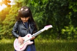 A confident young woman striking a pose with her electric bass guitar outdoors.
