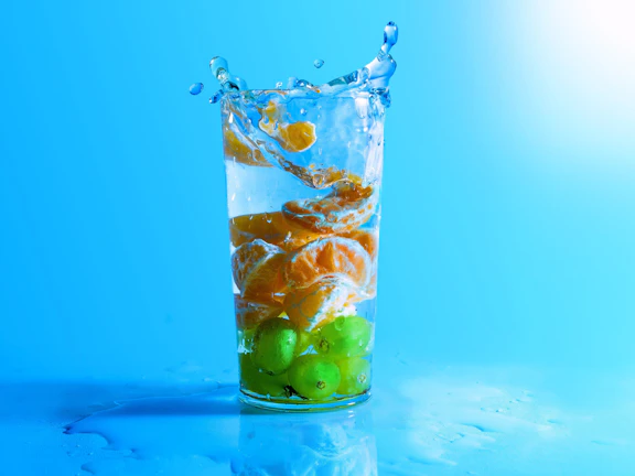 Close-up of clear mineral water pouring into a glass with fresh fruit slices nearby.