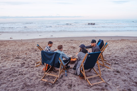 three men and one woman sitting on beach lounge in front fire pit near seashore in Tynemouth United Kingdom