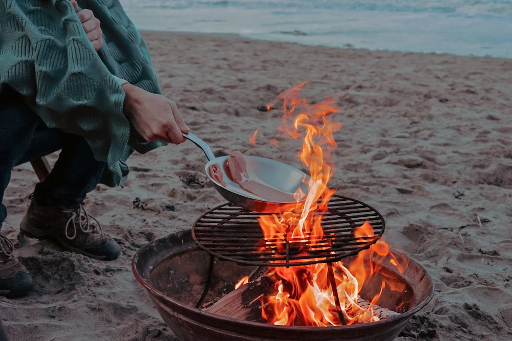 person cooking meat on bonfire near shoreline
