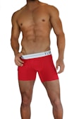 A muscular male torso is displayed, wearing bright red boxer briefs with a white waistband. The waistline of the briefs has a brand logo visible on it. The skin tone is tanned and the individual is posed in a confident stance.