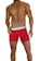 A muscular male torso is displayed, wearing bright red boxer briefs with a white waistband. The waistline of the briefs has a brand logo visible on it. The skin tone is tanned and the individual is posed in a confident stance.