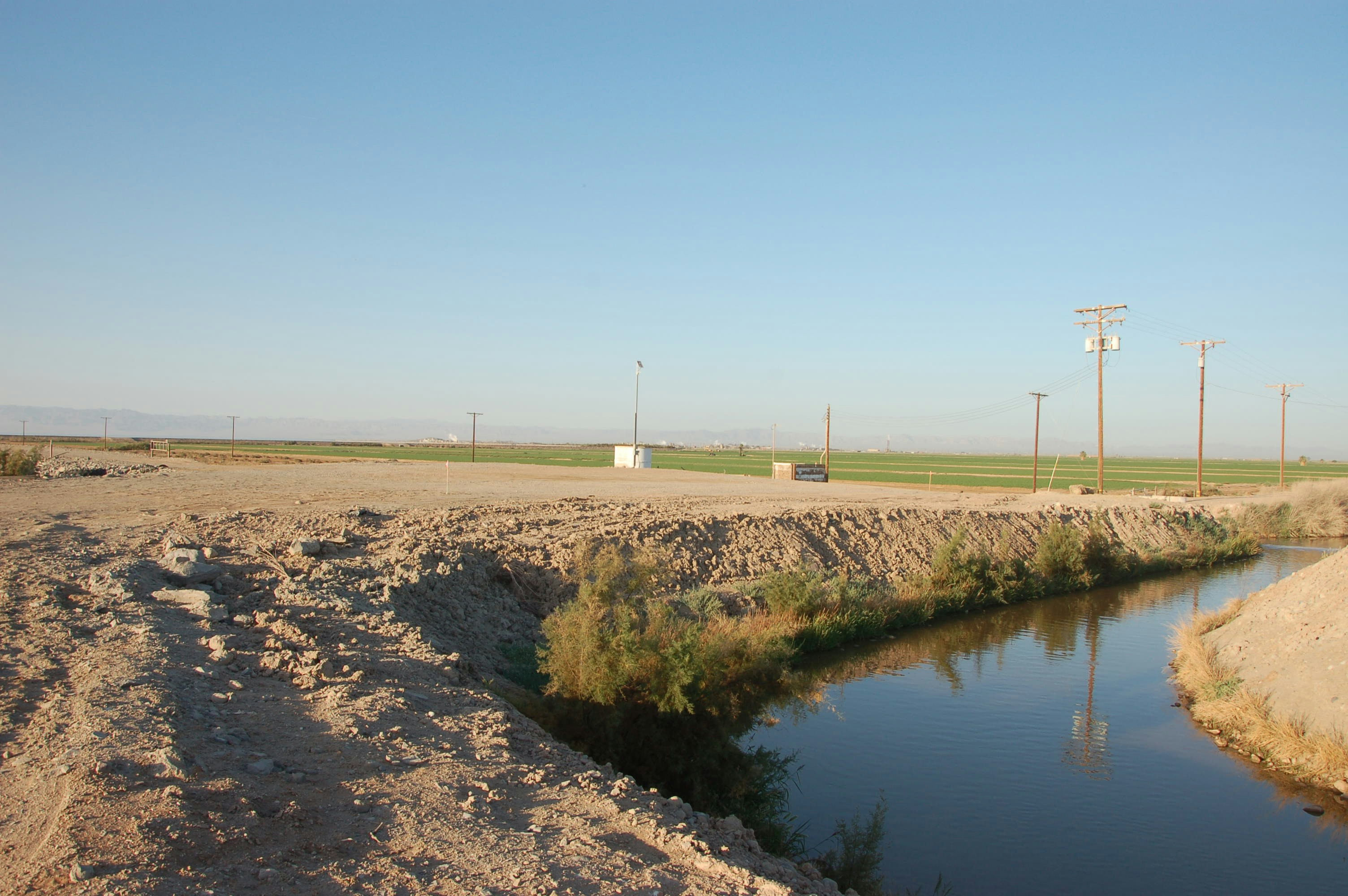 Irrigation canal with water flowing through agricultural fields, bright daylight, lush green crops on both sides