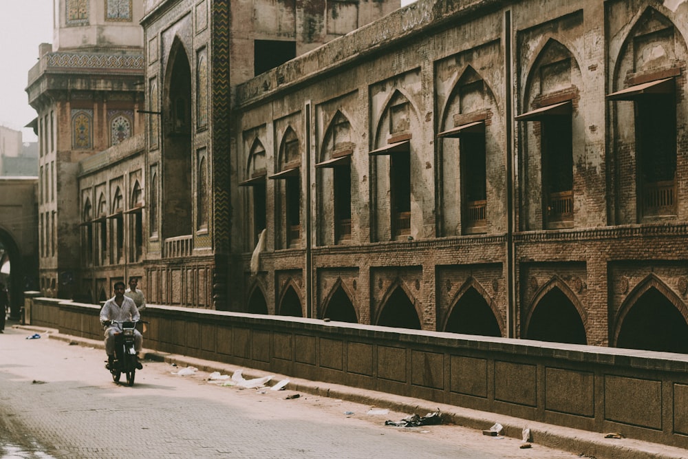 man riding motorcycle beside building during daytime