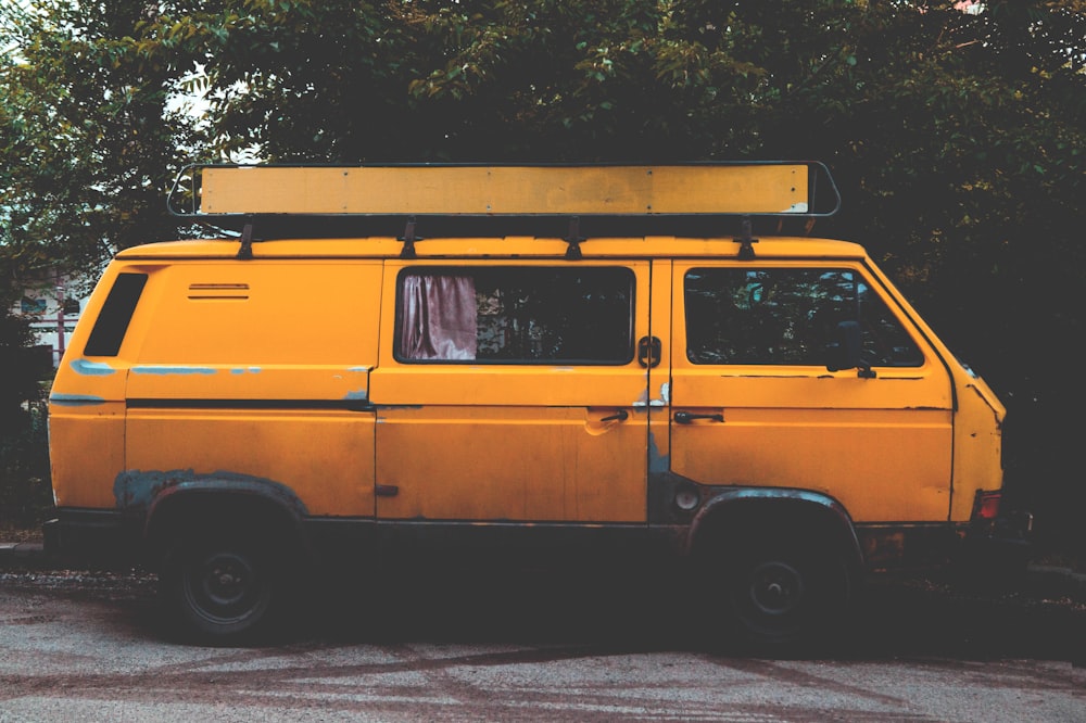 yellow panel van parked near green leafed trees