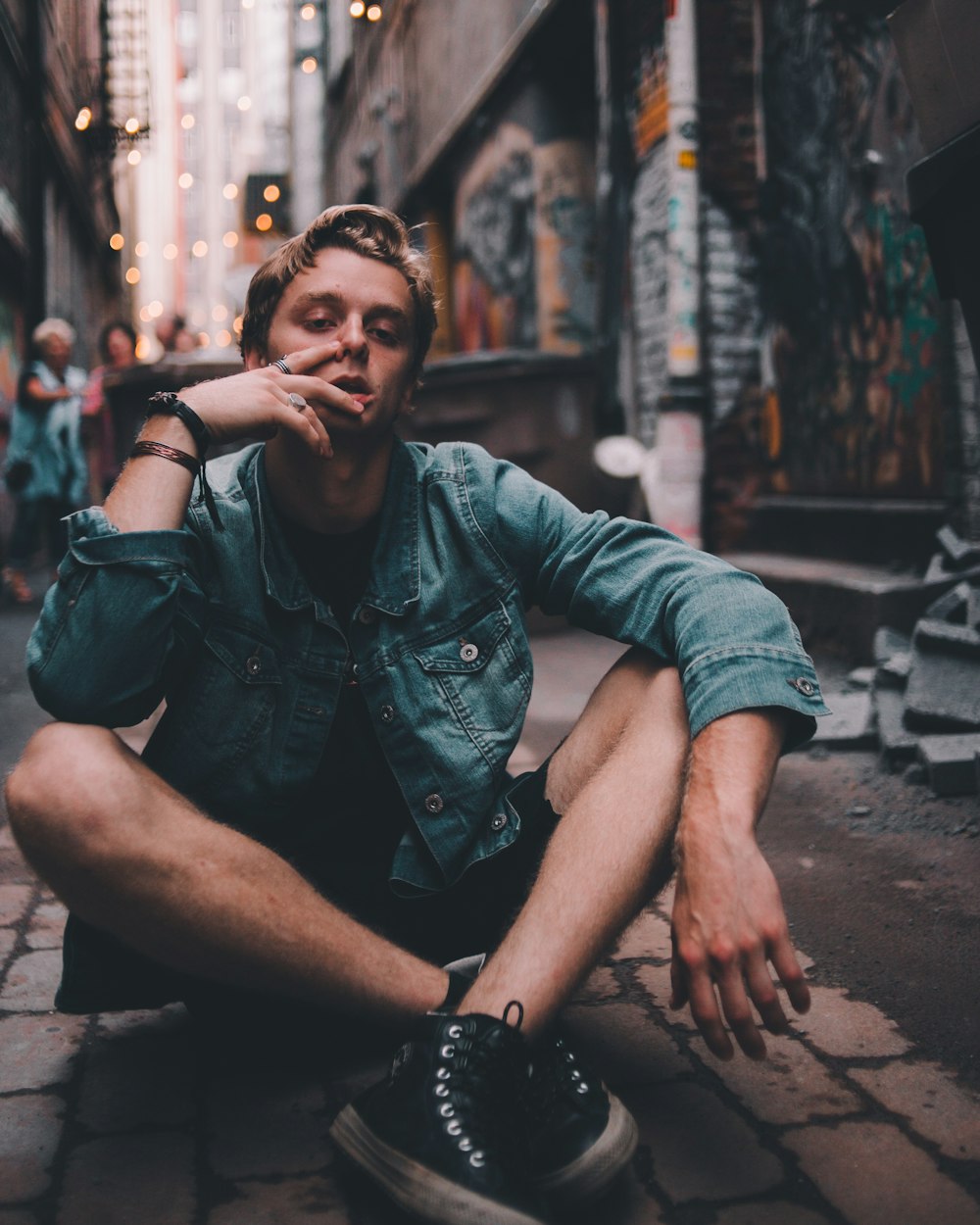 man sitting on alley near graffiti printed wall