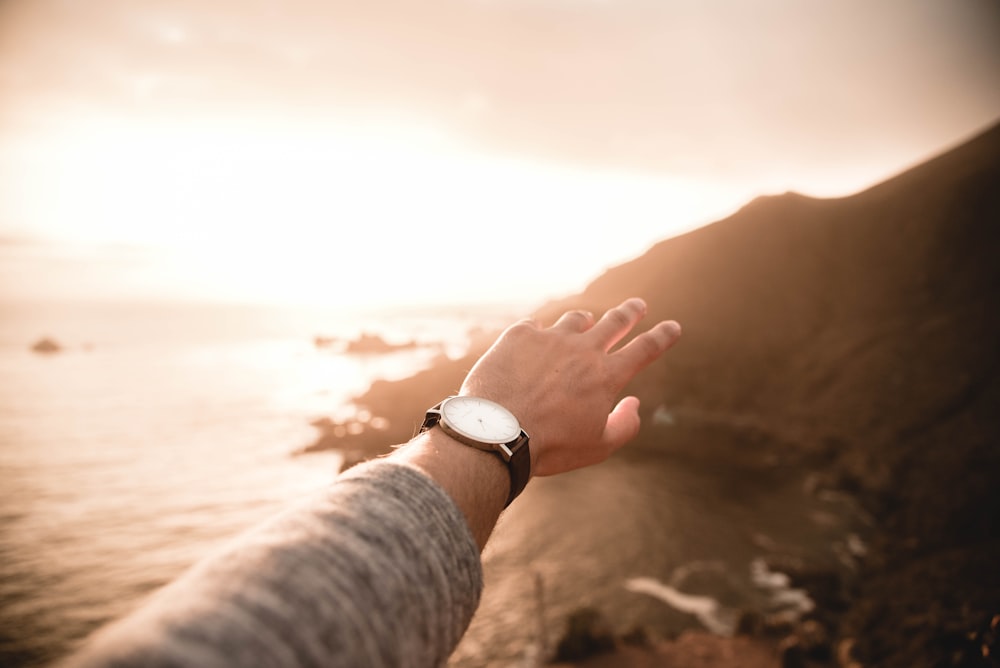 left person's arm wearing watch pointing body of water