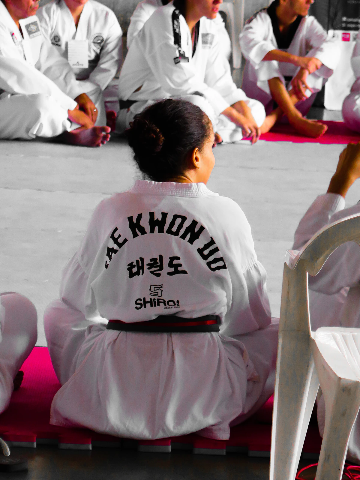 A young girl in a taekwondo dobok sitting on the mat, waiting for her turn
