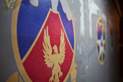 A close-up view of a colorful emblem featuring a stylized golden eagle on a red and blue shield set against a gray background. To the right, there are additional emblems, including a star design, partially visible.