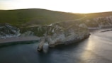 Sunset view of Durdle Door arch with travelers taking photos on the beach.