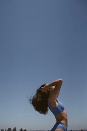 An athletic young woman outdoors, arms open wide, radiating vitality and energy against a clear blue sky.
