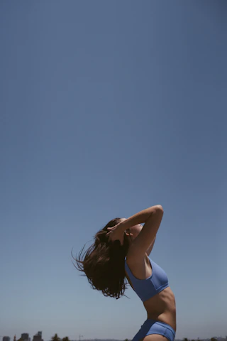 An athletic young woman outdoors, arms open wide, radiating vitality and energy against a clear blue sky.