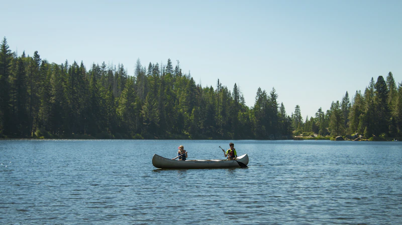 Campers paddling a red canoe across the sparkling lake