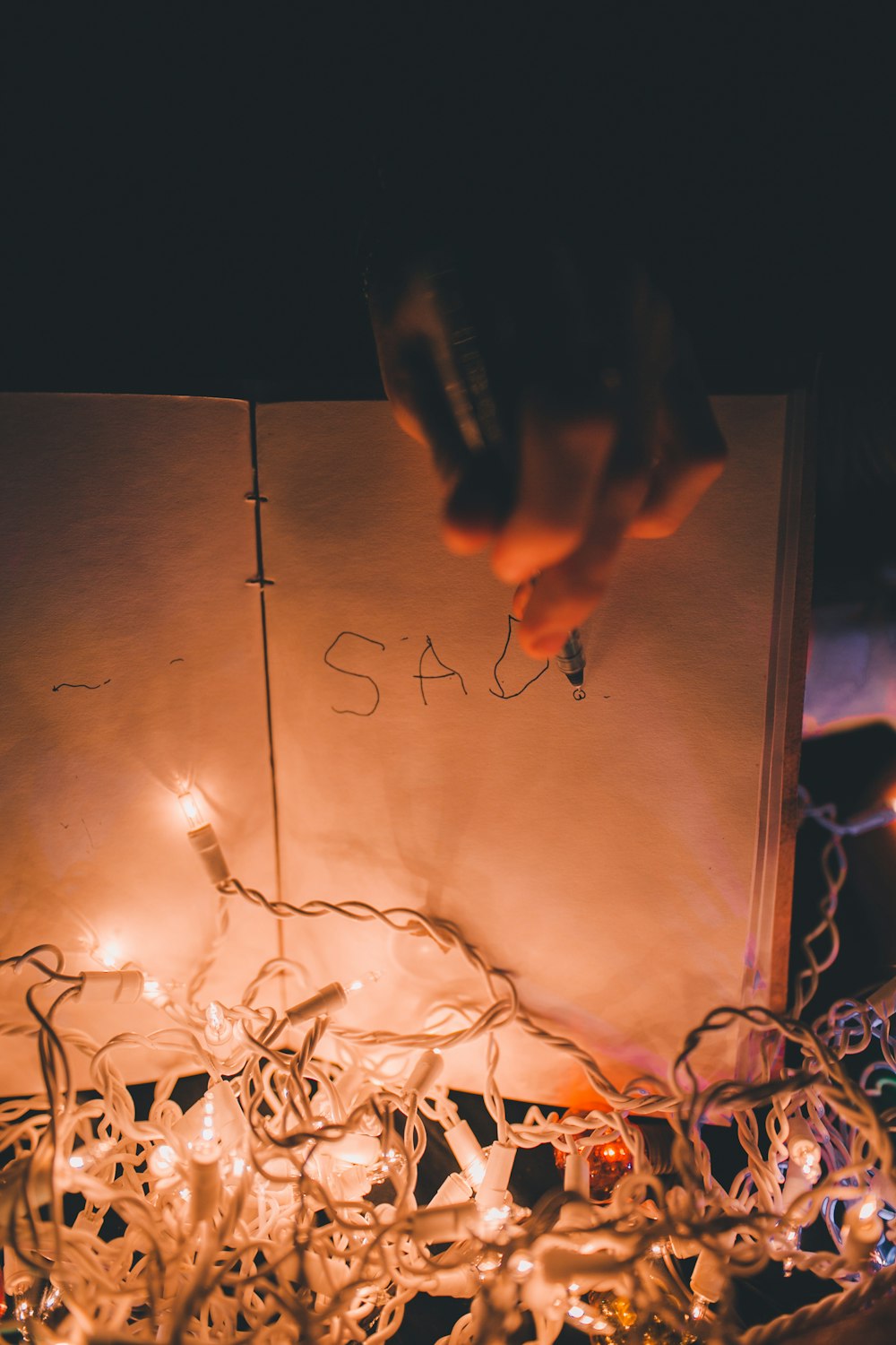person writing on book with lighted string lights