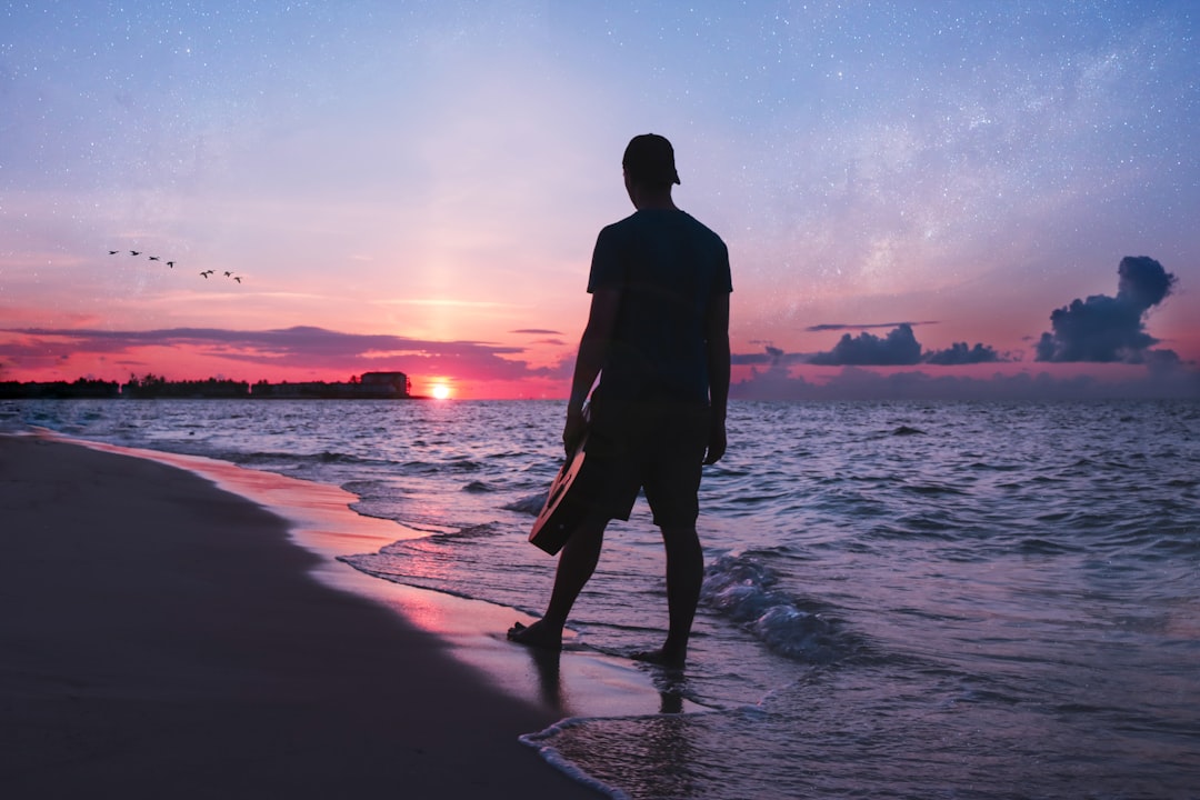 man holding guitar walking on shoreline