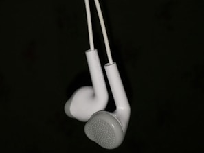 A pair of white earphones suspended against a dark background, showcasing their intricate design and smooth texture.